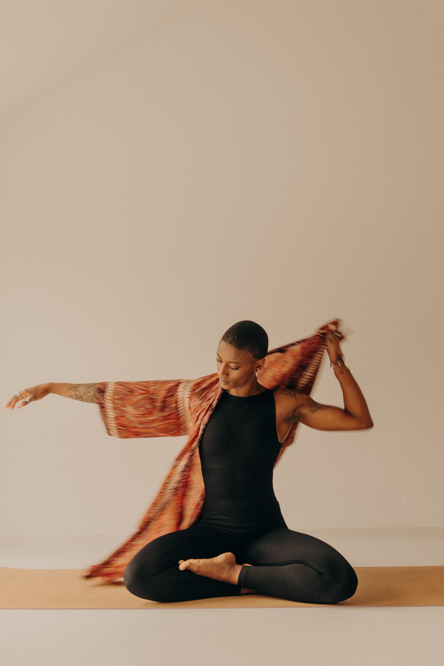 Femme noire en combinaison noire, assise en tailleur, enfilant un kimono avant un cours de Yoga Vinyasa à Orléans